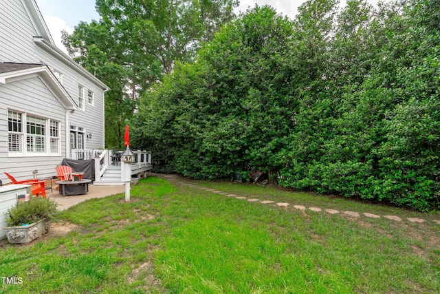 view of green lawn with a fire pit, a wooden deck, and a patio area