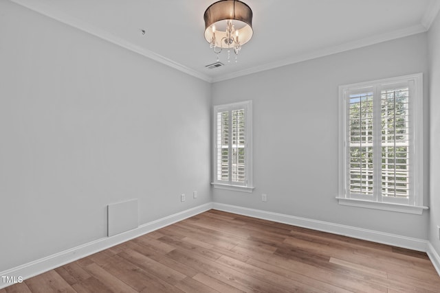 empty room featuring plenty of natural light, hardwood / wood-style flooring, a chandelier, and ornamental molding