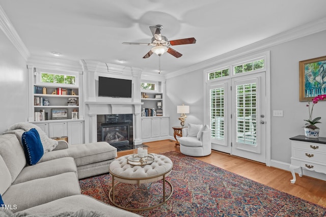living room with crown molding, ceiling fan, wood finished floors, a premium fireplace, and baseboards