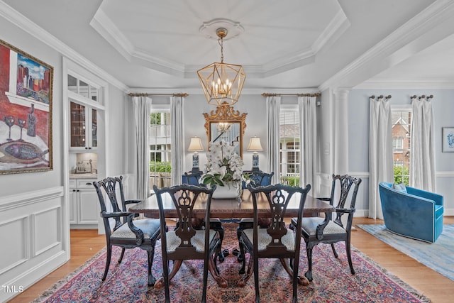 dining area featuring a chandelier, light wood-type flooring, crown molding, a tray ceiling, and a wainscoted wall