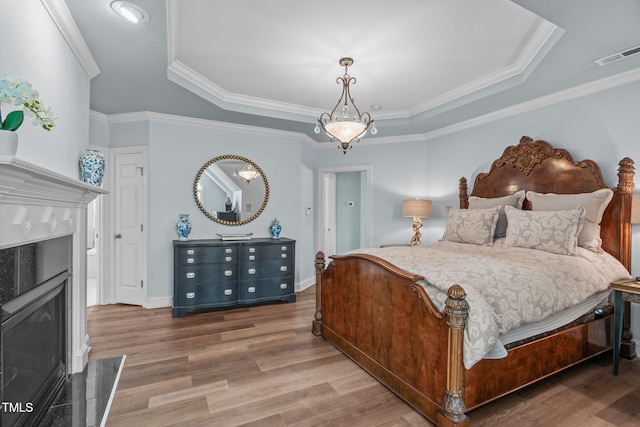 bedroom with a premium fireplace, light wood finished floors, a raised ceiling, crown molding, and baseboards