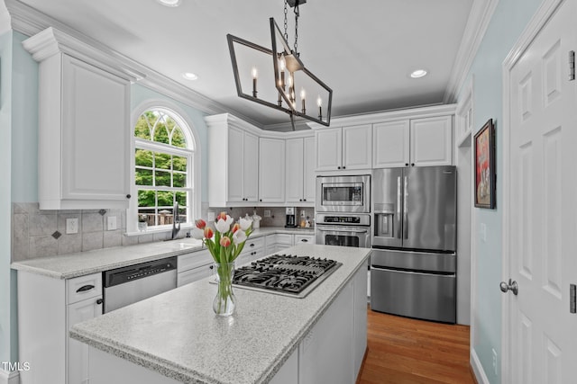 kitchen with appliances with stainless steel finishes, a center island, a sink, white cabinets, and ornamental molding