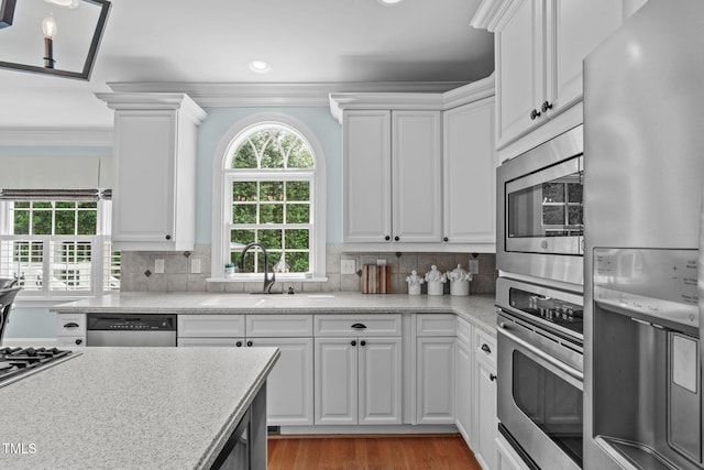 kitchen featuring appliances with stainless steel finishes, light countertops, white cabinets, a sink, and crown molding