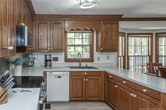 kitchen featuring white dishwasher, a textured ceiling, plenty of natural light, a sink, and a peninsula