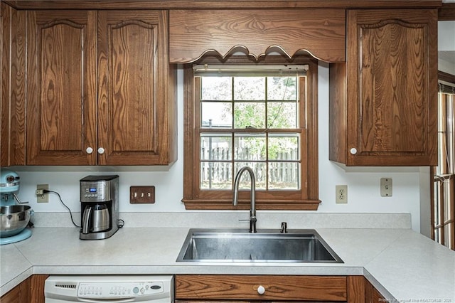 kitchen with light countertops, brown cabinets, white dishwasher, and a sink