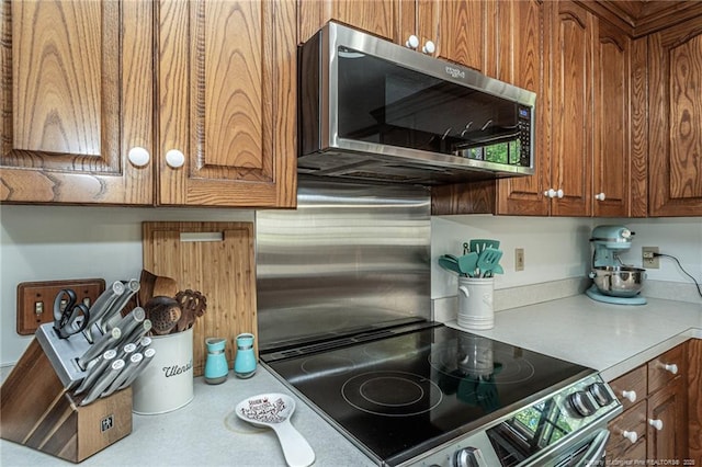kitchen featuring brown cabinets, electric range, stainless steel microwave, backsplash, and light countertops