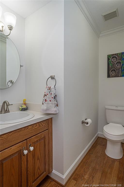 half bathroom featuring toilet, visible vents, vanity, crown molding, and wood finished floors