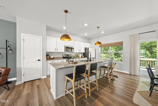 kitchen featuring stainless steel appliances, an island with sink, wood finished floors, white cabinetry, and a breakfast bar