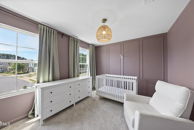 bedroom featuring light carpet, a nursery area, and a decorative wall