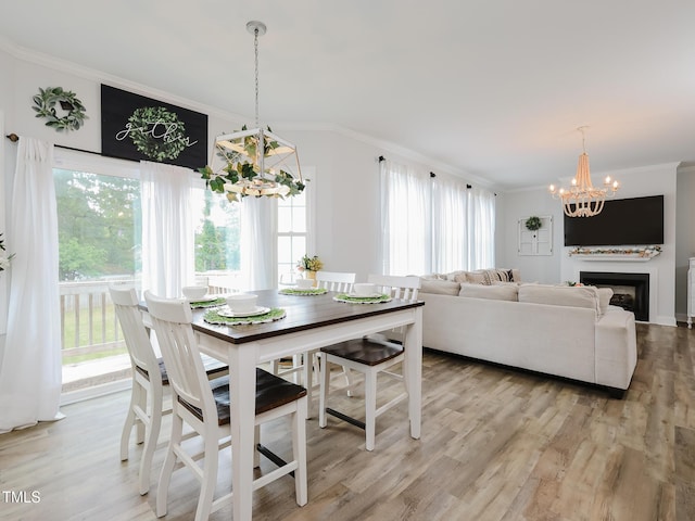 dining space with a chandelier, crown molding, light wood-style floors, and a fireplace
