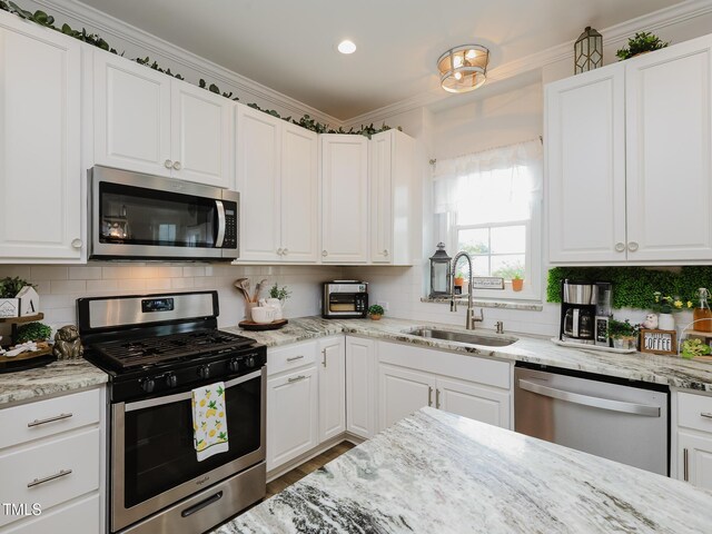 kitchen with appliances with stainless steel finishes, a sink, white cabinets, backsplash, and ornamental molding