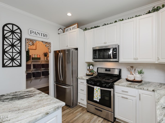 kitchen with stainless steel appliances, light wood-style flooring, white cabinets, ornamental molding, and tasteful backsplash