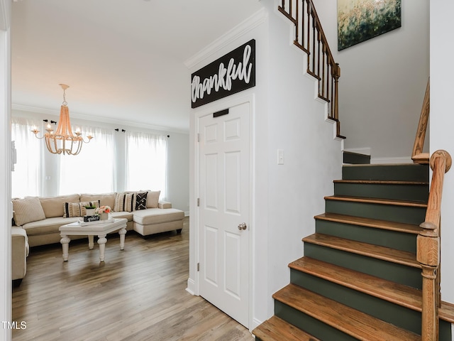 stairs featuring ornamental molding, a chandelier, and wood finished floors