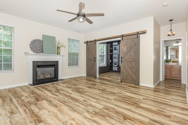 12340 Tetons Ct, Durham, NC 27703 - unfurnished living room with a barn door, light wood-style floors, a ceiling fan, a glass covered fireplace, and plenty of natural light