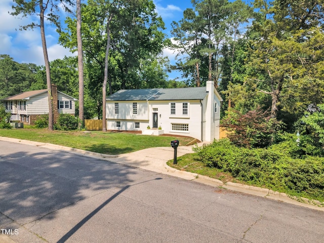 bi-level home with driveway, a chimney, and view of wooded area