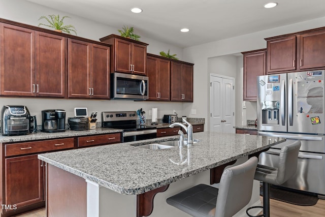 kitchen with appliances with stainless steel finishes, a sink, recessed lighting, a breakfast bar area, and a kitchen island with sink