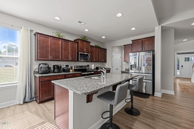 kitchen with stainless steel appliances, a sink, light wood-style flooring, a breakfast bar area, and baseboards