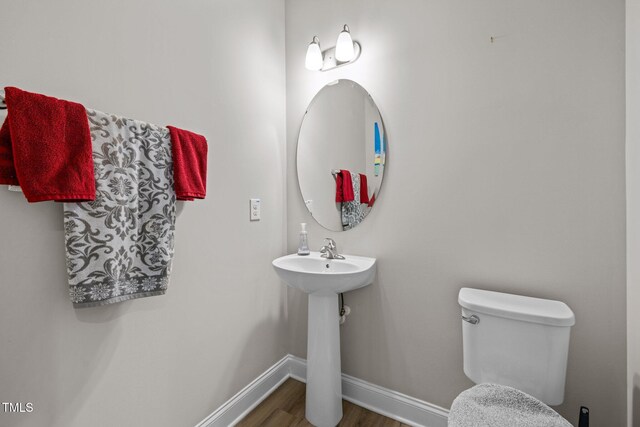 half bathroom with baseboards, wood finished floors, toilet, and a sink