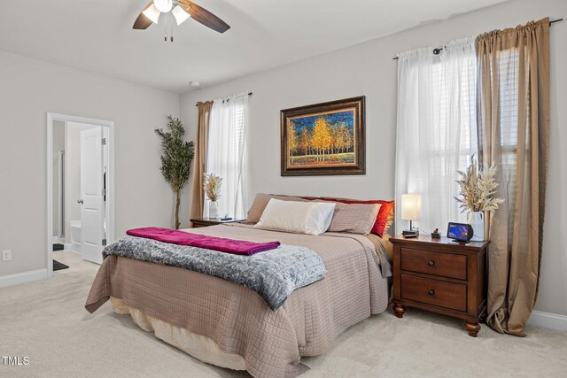 bedroom featuring light carpet, baseboards, ensuite bath, and ceiling fan
