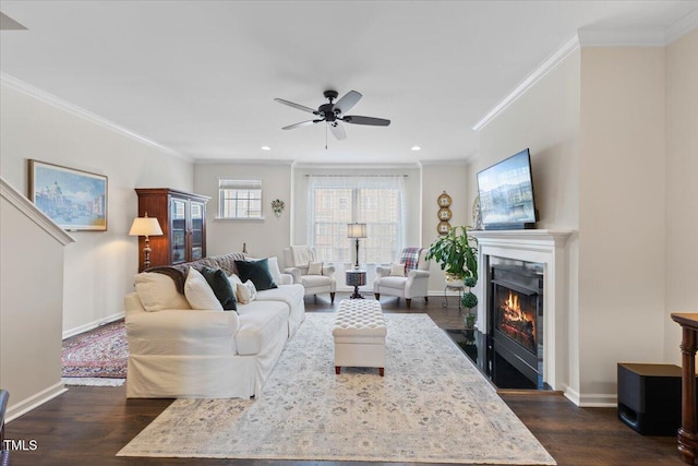 living room featuring dark wood-style floors, a fireplace with flush hearth, crown molding, baseboards, and a ceiling fan