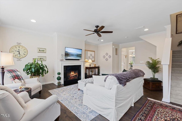 living room with dark wood-style flooring, recessed lighting, a ceiling fan, a glass covered fireplace, and crown molding