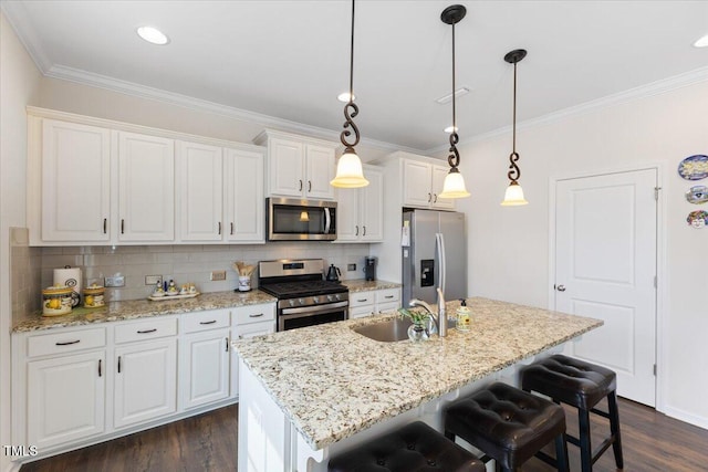 kitchen with appliances with stainless steel finishes, ornamental molding, white cabinets, a sink, and a kitchen island with sink