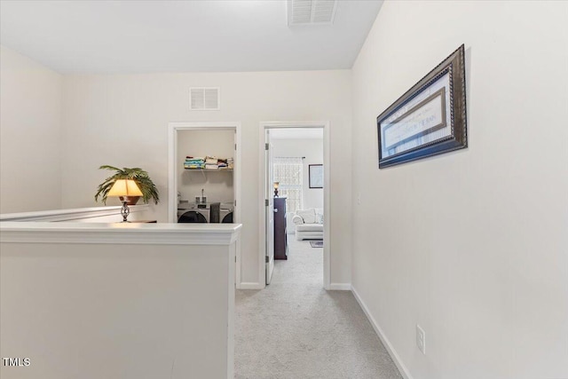 hallway featuring washing machine and dryer, light colored carpet, and baseboards