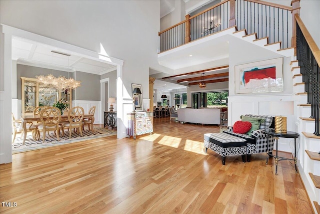 living area with a towering ceiling, wood finished floors, a decorative wall, stairs, and a chandelier