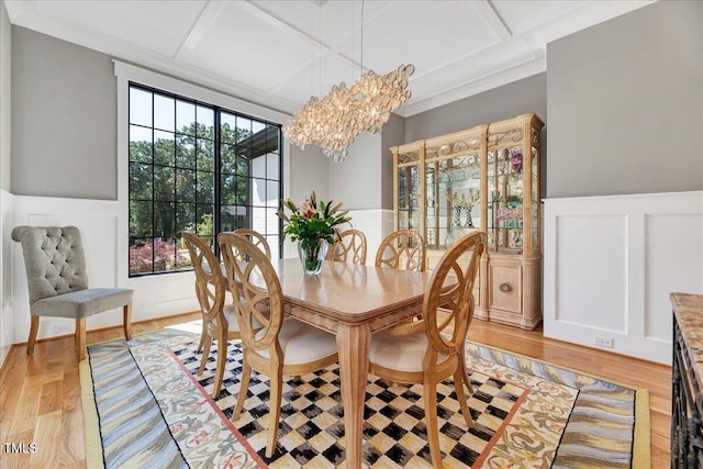 dining space featuring coffered ceiling, a decorative wall, light wood-style floors, a chandelier, and wainscoting