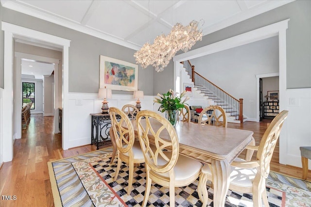 dining space featuring stairway, coffered ceiling, light wood finished floors, a chandelier, and wainscoting