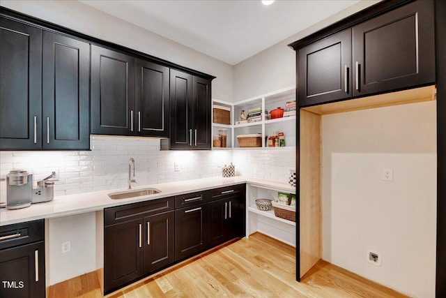 kitchen with a sink, decorative backsplash, light wood-type flooring, light countertops, and open shelves