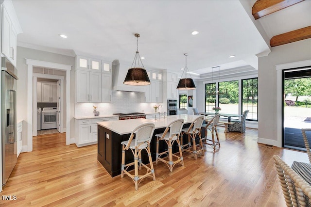 kitchen with stainless steel built in refrigerator, light countertops, white cabinets, a breakfast bar area, and light wood-style floors