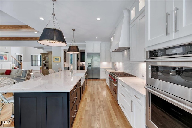 kitchen featuring high end appliances, premium range hood, white cabinetry, a sink, and light wood-style floors