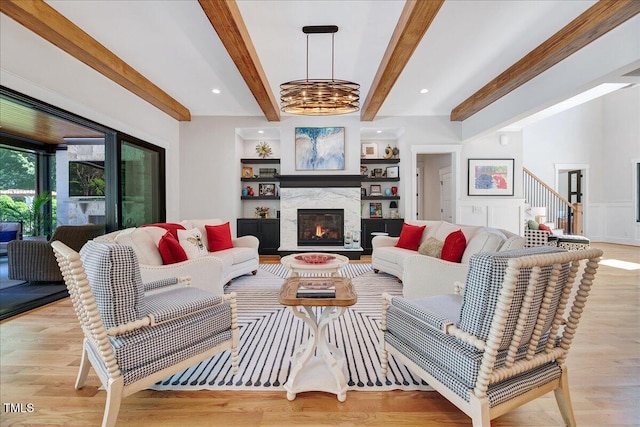 living area with light wood-style floors, a warm lit fireplace, beamed ceiling, and stairs