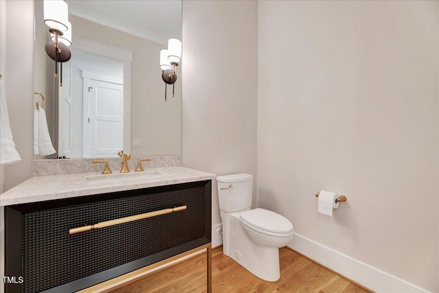 bathroom with toilet, wood finished floors, vanity, crown molding, and baseboards