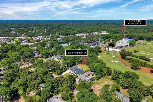 view of property location with a heavily wooded area, a golf club, and nearby suburban area