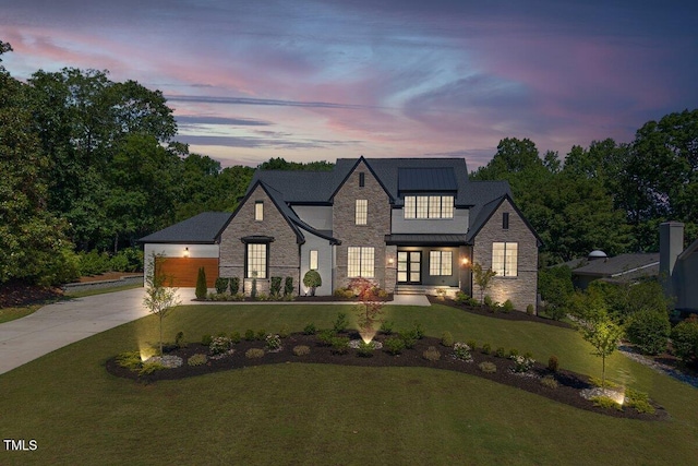 view of front facade with stone siding, a lawn, driveway, a garage, and french doors