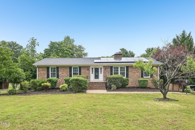 ranch-style home featuring roof mounted solar panels, brick siding, a chimney, and a front yard