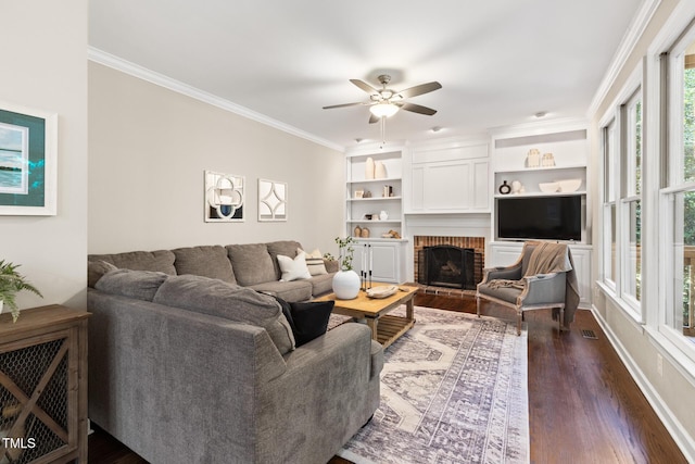 living area with dark wood-type flooring, ceiling fan, a brick fireplace, and ornamental molding