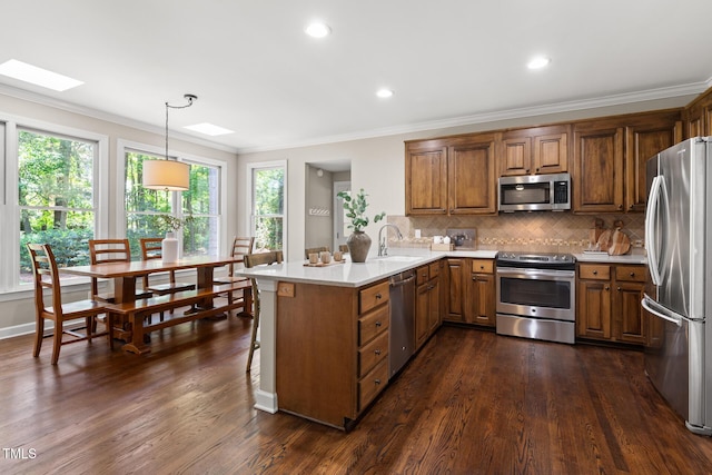 kitchen with stainless steel appliances, a skylight, brown cabinetry, healthy amount of natural light, and ornamental molding