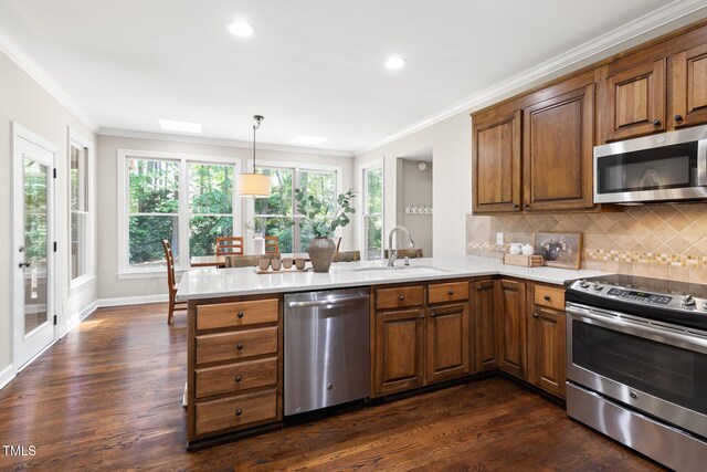 kitchen with stainless steel appliances, a sink, brown cabinetry, crown molding, and a peninsula