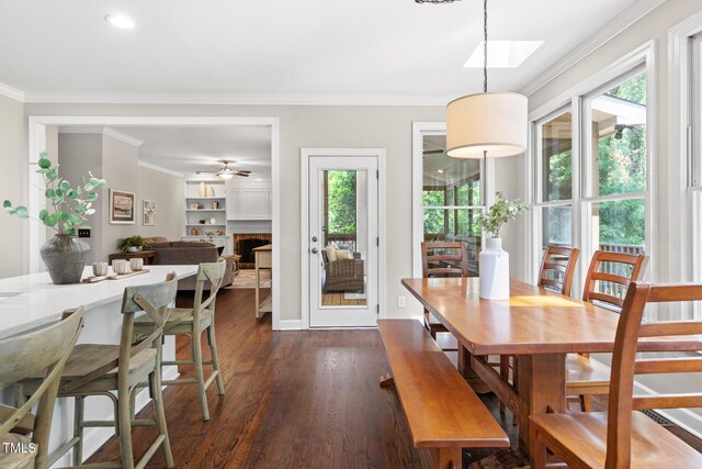 dining room featuring crown molding, dark wood finished floors, a ceiling fan, a skylight, and a brick fireplace