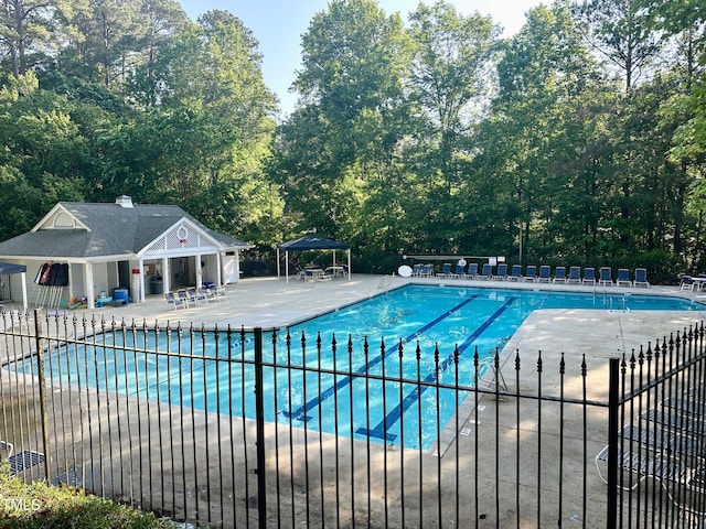community pool with fence, a patio, and view of scattered trees