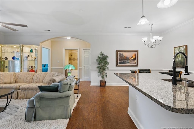 living room featuring ceiling fan with notable chandelier, baseboards, arched walkways, ornamental molding, and dark wood-style floors