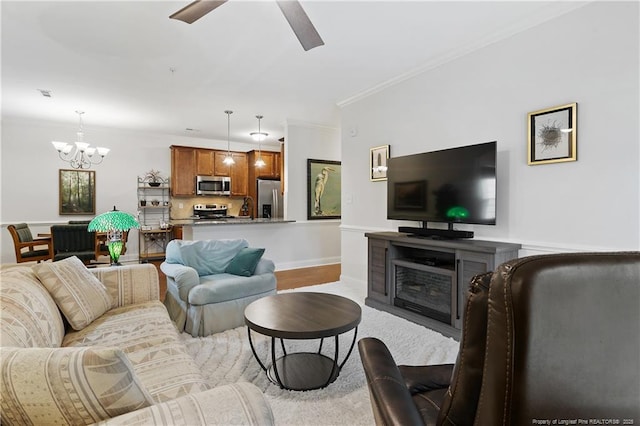 living area with baseboards, wood finished floors, ceiling fan with notable chandelier, and ornamental molding