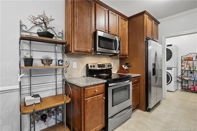 kitchen featuring ornamental molding, light stone counters, stacked washer and clothes dryer, decorative backsplash, and appliances with stainless steel finishes