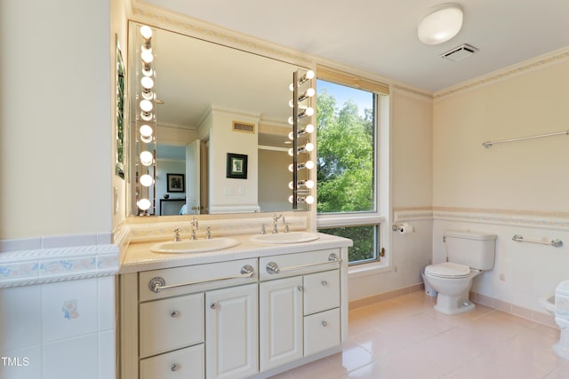 bathroom featuring toilet, double vanity, wainscoting, crown molding, and tile patterned floors