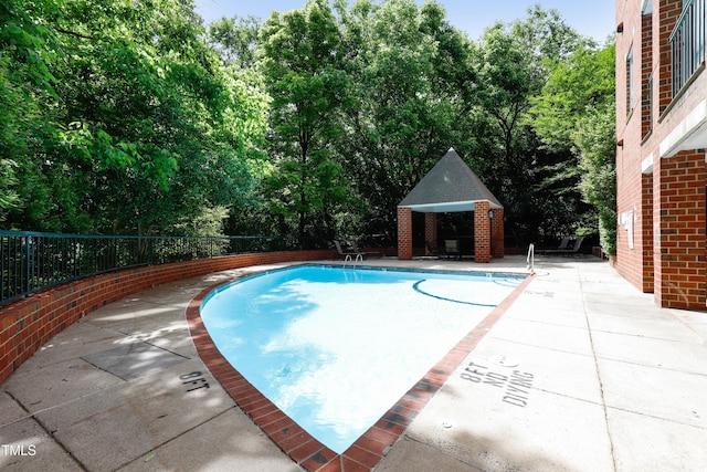 community pool featuring fence, a patio area, view of wooded area, and a gazebo