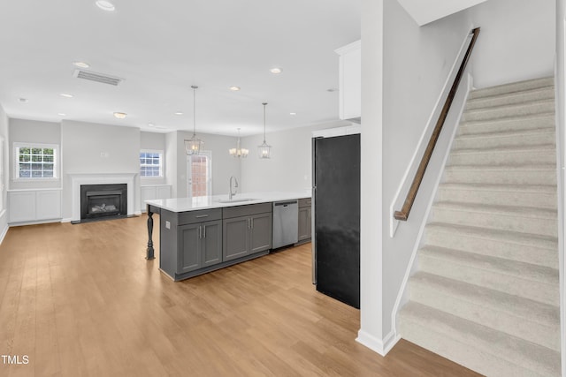 kitchen featuring stainless steel appliances, gray cabinetry, light wood-style flooring, light countertops, and a fireplace with flush hearth