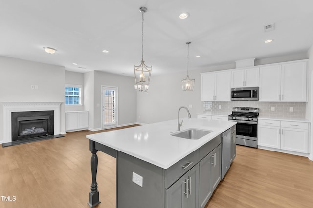 kitchen featuring appliances with stainless steel finishes, a sink, gray cabinetry, light countertops, and white cabinetry